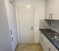 White walls, wooden floor, white kitchen cabinets, marble countertop, stainless steel sink, dishwasher, washing machine