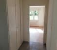 Empty hallway with double doors, tiled floor, white walls, sunlight from the window, and a radiator