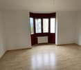 Empty room with wooden floor, three windows, radiator, and no furniture