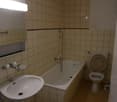 Tiled walls, tiled floor, bathtub, toilet, sink, and overhead lighting.