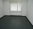 An empty room with white walls, a white radiator, a large window, and gray flooring