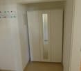 Empty room with white wardrobe with mirror, tiled floor, hooks on the wall