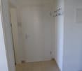 Corridor with white walls, white tile flooring, white door, power outlet, coat rack on the wall