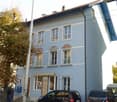 3 story blue house with multiple windows, awning over door, cars parked in front