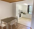 Dining area with a wooden table and white chairs, white kitchen with appliances, wooden ceiling, tiled floor