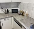 modern kitchen with white cabinets, gray countertops, dishwasher, microwave, electric kettle, coffee pods, cups, and a sink