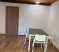 small room with wooden floors, white walls, wooden ceiling, table with 4 chairs, white table, wooden door