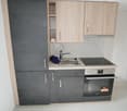 Compact kitchen with light wood cabinets, gray countertops, built-in oven, and a dishwasher