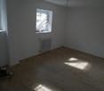 Empty room with hardwood flooring, gray walls, and a window providing natural light. The room appears to be in the process of renovation or preparation for new occupancy.