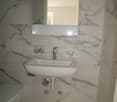 Bathroom with white marble tiles, white sink, silver faucet, mirror, and white toilet.