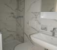 Bathroom with white marble tiles, shower, toilet, sink, mirror, and faucet