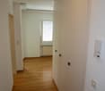 Empty hallway with wooden floor, white walls, built-in wardrobes, window with blinds, power outlets, and a radiator.