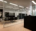 Large open office space with glass walls, black furniture and storage units, and a large abstract artwork on the wall.