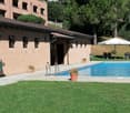 brick house, swimming pool, large umbrellas, chairs, green lawn, potted plants