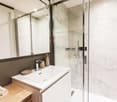 Modern bathroom with marble-like walls, a white vanity with a sink, a glass shower enclosure, and towels on a wooden bench.