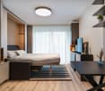 Spacious bedroom with large windows, hardwood flooring, built-in storage, and a modern TV stand. The room features a comfortable bed, striped rug, and decorative accents.