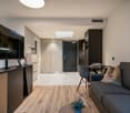 Open-plan studio apartment with hardwood flooring, gray sofa, dining table, TV stand, and kitchen area with dishwasher