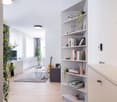 Spacious living room with white walls, hardwood floors, large windows, built-in shelving unit, potted plants, guitar, and a couch