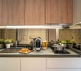 Modern kitchen with wooden cabinets, stainless steel appliances including a coffee maker and dishwasher, potted plants, and various cooking utensils and ingredients on the countertop.