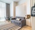 Spacious living room with large windows, gray sofa, striped rug, dining table, and a large tote bag with text on it.