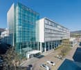 Large modern glass and steel office building with multiple floors, parking spaces in front of the building