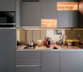 Modern kitchen with gray cabinets, wooden countertop, built-in Siemens microwave oven, various kitchen appliances and utensils, and open shelving with decorative items