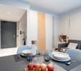The image shows a modern and stylish open-plan living and dining area. The space features a gray sofa, a dining table with place settings, and a kitchen area with a dishwasher visible. The walls are a mix of white and wood paneling, creating a warm and in