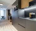 modern kitchen with wooden floor, granite countertops, built-in appliances, microwave, stove, and refrigerator, wooden cabinets