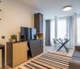 Spacious living room with large windows, wooden shelves, TV stand, desk, sofa, and striped rug