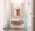 Modern bathroom with white walls, glass shower enclosure, vanity with sink, and wooden accents.