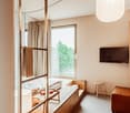 small room with bed, window, TV, stool, couch, lamp, tray, and wooden cabinet