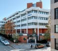 Multi-story commercial building with a mix of brick and glass facade, parking spaces in front, and some trees and landscaping around the building.