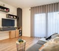 Minimalist decor, wooden floor, large windows with curtains, TV unit, couch, center table, lamp