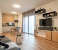 modern open plan living room, wooden floor, gray couch, wooden dining table, TV on entertainment unit, open kitchen with breakfast bar