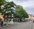 large store building with many signs and windows, street lamps, people, parked bicycles, trees