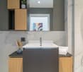 modern bathroom, marble tiles, white sink, wooden cabinets, shower enclosure, mirror, power outlet, toilet paper holder