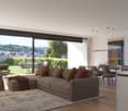 Spacious open-plan living room with large windows offering a scenic view of the surrounding mountains and cityscape. The room features a comfortable L-shaped sofa, a dining table with chairs, and a modern kitchen area with shelving and appliances. The dec