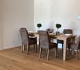 The image shows a modern and stylish dining room with a wooden dining table and six brown leather chairs. The room has a minimalist and clean design, with white walls and hardwood floors. There are two small potted plants on the table, adding a touch of g