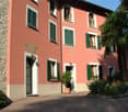 2 story house, red brick, white windows, green shutters, brown door, garden, plants, cobblestone road