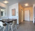 modern kitchen with table, white dining chairs, open concept design, contemporary wall decorations, natural light from windows, open door leading to another room