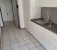 Compact kitchen with white cabinets, gray countertop, tiled floor, and a stainless steel sink with a dishwasher visible.