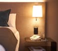 a bed with pillows, nightstand with books and pen, wall-mounted lamp