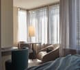hotel room, beige decor, wooden floor, windows with curtains, comfortable chairs, desk, bed