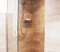 Spacious shower area with glass door, tiled walls in beige and brown tones, shower head and fixtures, towel shelf