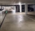 underground parking lot, with 2 cars parked, multiple white pillars, lights on ceiling