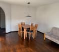 A room with a dining table and 6 chairs, a couch, hardwood floor, white walls, and a pendant light.