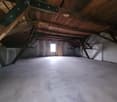 empty attic room with wooden beams, concrete floor, small window, door