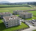 Three apartment buildings, green lawn, parking lot, solar panels on the roofs