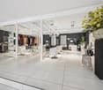 Interior of a salon with chairs, mirrors, and plants. White tiled floor, glass partitions, bright lighting.