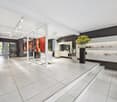 Modern beauty salon with clean and minimal design, white tile flooring, glass partitions, art paintings, furniture, and plants.